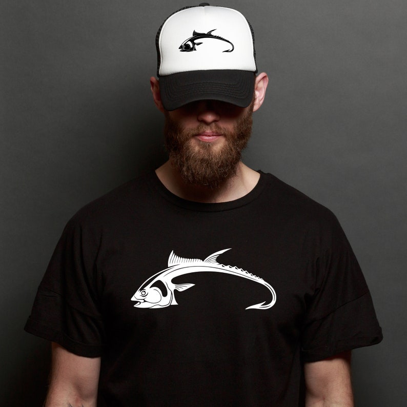 May include: A black t-shirt with a white graphic of a fish with a hook for a tail. The person is wearing a black and white trucker hat with a fish graphic.