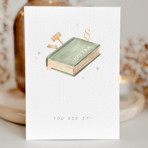 Könnte beinhalten: Eine Grußkarte im Aquarellstil mit einem grünen Buch mit der Aufschrift "Helena" und einer Hammer-Illustration. Der Text "YOU DID IT!" steht unten. Die Karte hat einen hellen Hintergrund mit kleinen, farbigen Punkten.