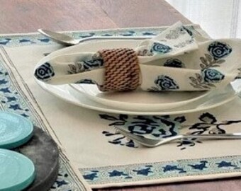 May include: A teal blue metal candle holder with two candle holders on a wooden table with a white tablecloth with a blue floral pattern. 