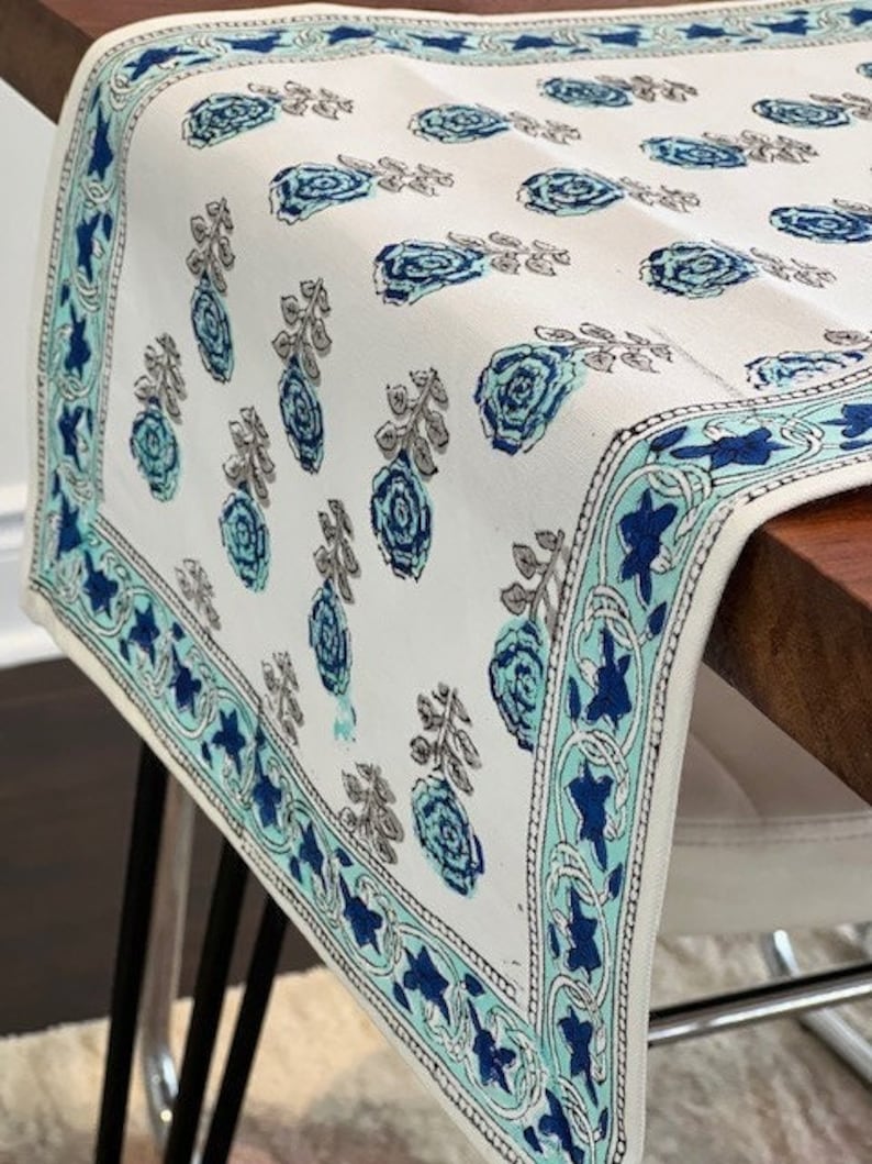 May include: White table runner with a blue and green floral pattern. The runner has a decorative border with a blue and green floral design.