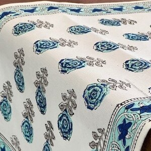 May include: White table runner with a blue and green floral pattern. The runner has a border with a repeating design of blue and green leaves and flowers.
