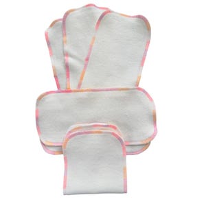 May include: A stack of white, rectangular cloth diaper inserts with rounded corners. Each insert has a colorful border of pink, orange, and yellow stitching. The inserts are arranged in a fan-like pattern against a white background.