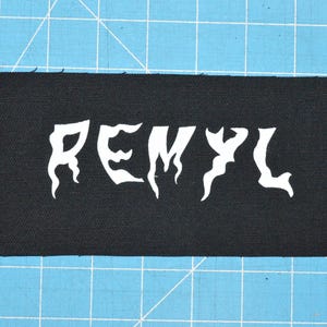 Pode incluir: Remendo de tecido preto com a palavra "REMYL" em letras brancas estilizadas.