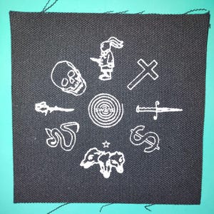 Puede incluir: Parche cuadrado de tela negra con diseños bordados en blanco. Presenta una calavera, una figura con orejas de conejo, una cruz, una daga, un signo de dólar, una estrella, una vaca, una serpiente y una espiral con la palabra "swans".