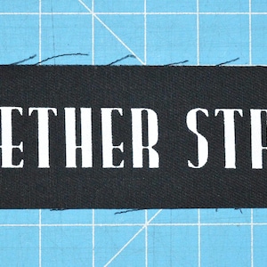 Può includere: Toppa in tessuto nero con testo bianco che recita "LEATHER STRIP".