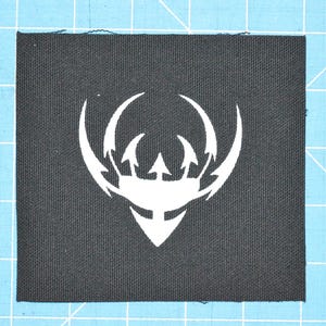 Puede incluir: Parche de tela negro con un diseño estilizado blanco de un tridente con tres puntas. El diseño está rodeado por dos líneas curvas.