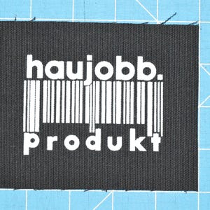 Pode incluir: Etiqueta de tecido preto com texto branco que diz "haujobb. produkt" e um código de barras.