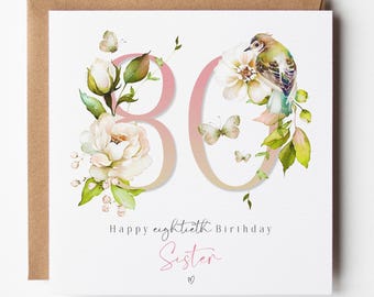 May include: A square greeting card with a brown envelope featuring the number 80 in a gradient pink and gold font. The design includes watercolor illustrations of white flowers, green leaves, small butterflies, and a bird, with the text Happy eightieth Birthday Sister.
