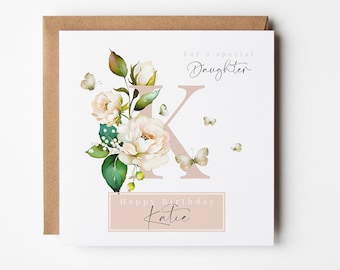 May include: A square greeting card with a floral design and the text "For a special Daughter" and "Happy Birthday Katie." The card features a large letter "K" and illustrations of butterflies and flowers. The card is set on a brown envelope.