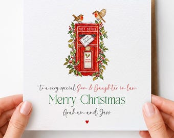 May include: A square white greeting card featuring a red post office box illustration surrounded by holly and two robins. Text reads: To a very special Son & Daughter in law, Merry Christmas, Graham and Jess, with a small red heart below.