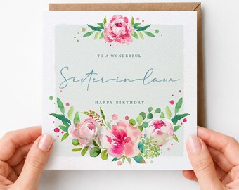 May include: A square greeting card with a light green background featuring watercolor pink peonies and green foliage. The text reads: TO A WONDERFUL Sister-in-law HAPPY BIRTHDAY. The card is set against a brown envelope, showcasing a floral design.