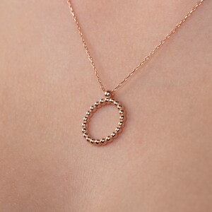 May include: A rose gold necklace with a circle pendant made of small beads.