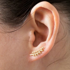 May include: Gold leaf ear cuff earring. The earring is shaped like a branch with small leaves. The earring is worn in the upper part of the ear.
