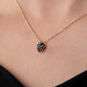 May include: A gold chain necklace with a small, black, heart-shaped pendant. The pendant is textured with small, raised dots.