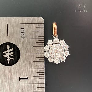 May include: A silver-toned pendant featuring a central round stone surrounded by a halo of ten smaller round stones, with a rose gold-toned bail. A metal ruler is positioned to the left, showing the pendant is approximately 0.5 inches wide.