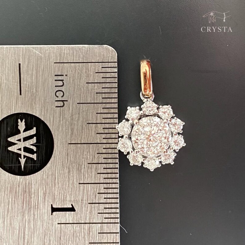 May include: A silver-toned pendant featuring a central round stone surrounded by a halo of ten smaller round stones, with a rose gold-toned bail. A metal ruler is positioned to the left, showing the pendant is approximately 0.5 inches wide.