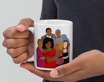 May include: White ceramic mug featuring a group illustration of people in various outfits. The illustration includes people with different skin tones and hairstyles. The mug is held by a person.