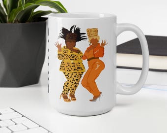 May include: White ceramic mug featuring a colorful illustration of two dancing figures. One figure is in a yellow leopard print outfit, and the other is in an orange jumpsuit. The mug has a large handle.