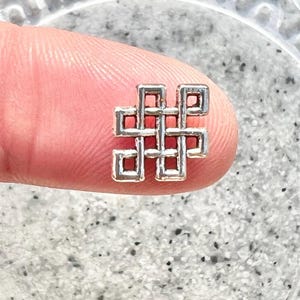 May include: A silver charm in the shape of a traditional endless knot, a symbol of good luck and eternity.