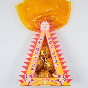 May include: A triangular box of "Exploding Bon-Bons" with a yellow and red design. The box contains several gold-wrapped chocolate candies. The top is covered in yellow cellophane. Text on the box reads "It is a real BOOM!"