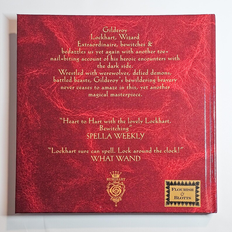 Puede incluir: Una cubierta de libro cuadrada con un fondo rojo profundo texturizado y texto dorado. El texto describe a Gilderoy Lockhart e incluye citas de Spella Weekly y What Wand. Un logotipo dorado y el emblema de Flourish & Blotts est&aacute;n en la parte inferior.