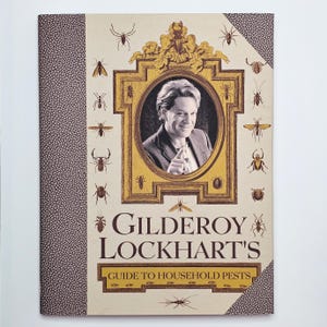 May include: A book titled "Gilderoy Lockhart's Guide to Household Pests" with a portrait of a man in a gold frame. The cover is beige with insect illustrations and a brown textured spine.