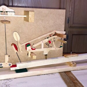 Può includere: Un modello in legno di un'azione di pianoforte, che mostra il meccanismo che collega i tasti ai martelli. Il modello è montato su una base in legno e include una leva in legno, una molla metallica e un martello in legno.
