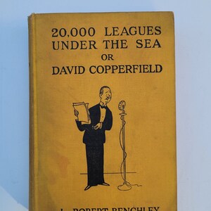 May include: A vintage book with a mustard-yellow cover. The title reads "20,000 Leagues Under the Sea or David Copperfield" by Robert Benchley. An illustration of a man in a tuxedo with a microphone is on the cover.