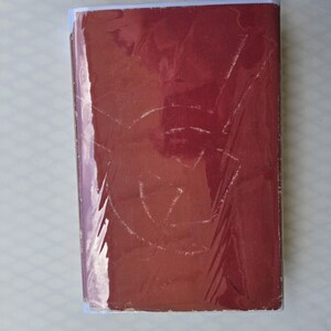 May include: A maroon book with a white spine and a clear plastic cover. The cover has a faded design. The book is rectangular and appears to be in good condition.