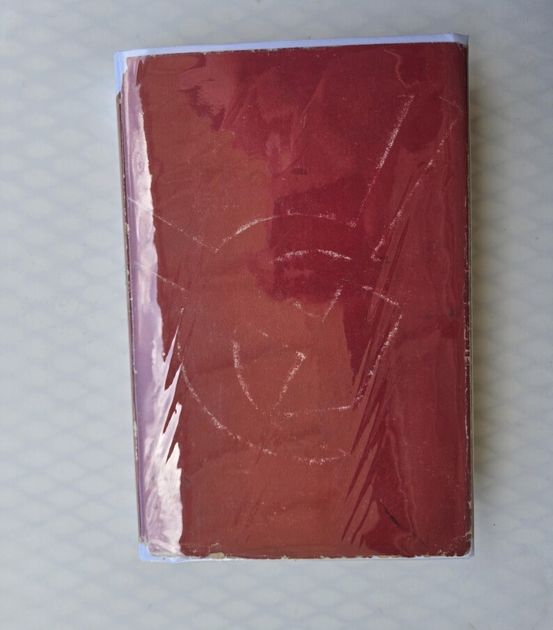May include: A maroon book with a white spine and a clear plastic cover. The cover has a faded design. The book is rectangular and appears to be in good condition.