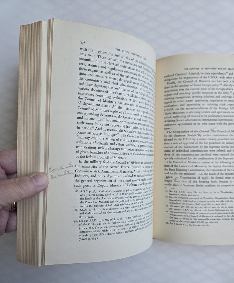May include: Open book with text on aged paper. The pages are yellowed, and the text is in black. A hand is holding the book open, revealing the text and the book's binding. The book appears to be a historical document.