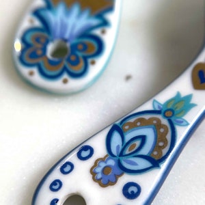 Ceramic white measuring spoons detail of handle with designer floral print in blue, green, and gold.