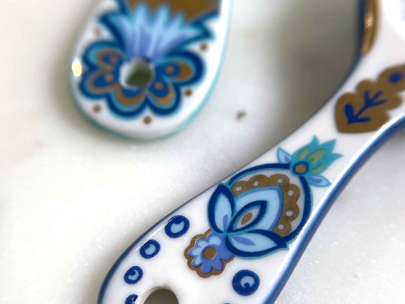 Ceramic white measuring spoons detail of handle with designer floral print in blue, green, and gold.
