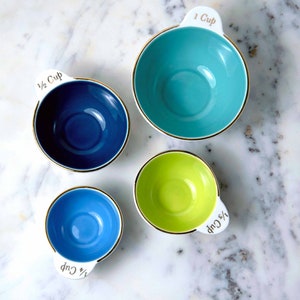 Nested ceramic measuring cups set with different colored interiors in blue, robin's egg blue, teal, and lime green.