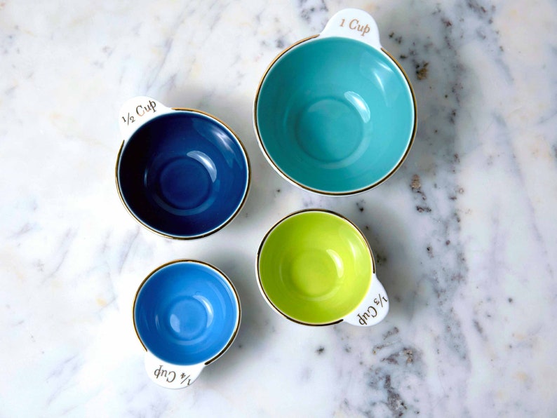 Nested ceramic measuring cups set with different colored interiors in blue, robin's egg blue, teal, and lime green.