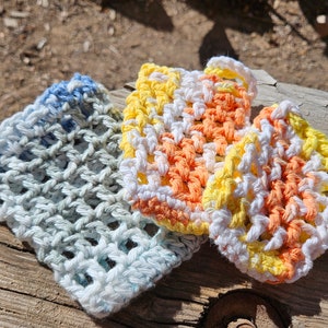 May include: Three crocheted dishcloths in different colors. One is blue and white, one is orange and white, and one is yellow and white.