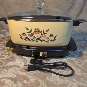 May include: A rectangular yellow slow cooker with a clear glass lid and black handles. The front features a graphic illustration of various mushrooms with green leaves. The base is black with a temperature control dial and a detachable power cord.