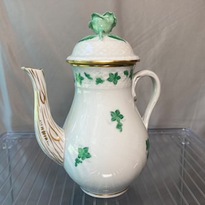 May include: A white porcelain coffee pot with a green and gold floral design. The pot has a lid with a green floral finial.