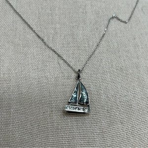 May include: Silver-toned necklace with a sailboat pendant. The pendant features a detailed sailboat design with a blue-green enamel sail and a row of clear crystals along the bottom. The chain is delicate and the pendant is approximately 1 inch in length.