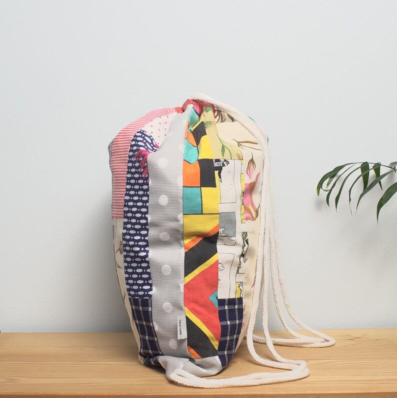 K&ouml;nnte beinhalten: Eine bunte Patchwork-Kordeltasche mit einem wei&szlig;en Kordelzug. Die Tasche besteht aus verschiedenen Stoffen mit verschiedenen Mustern, darunter Punkte, Streifen und Blumenmuster.