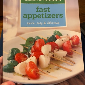 Könnte beinhalten: Ein Kochbuch mit dem Titel "meals in minutes fast appetizers quick, easy & delicious" mit einem Foto von Mozzarella- und Tomatenspießen auf einem weißen Teller.