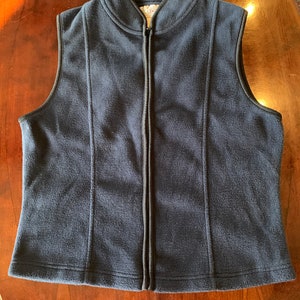 May include: A dark blue fleece vest with a zipper closure and a black collar. The vest has a small white tag with the text "EDC" on it.