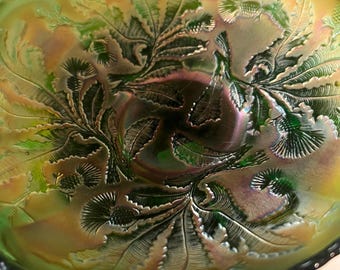 May include: An oval-shaped iridescent green carnival glass bowl featuring a raised relief pattern of thistle flowers and fern-like leaves. The bowl has a scalloped edge and displays a metallic sheen with golden and purple highlights across the surface.