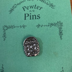 Puede incluir: Un pin de peltre plateado que representa una cesta llena de fruta. El pin está en una tarjeta verde con las palabras "Pewter Pins" impresas en ella.