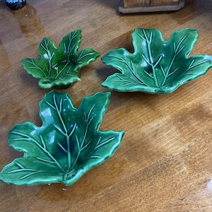 Puede incluir: Tres cuencos de cerámica verde en forma de hoja de arce. Los cuencos tienen un acabado brillante.