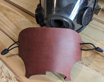 May include: A brown leather face mask with black elastic straps. The mask is designed to fit over a respirator.