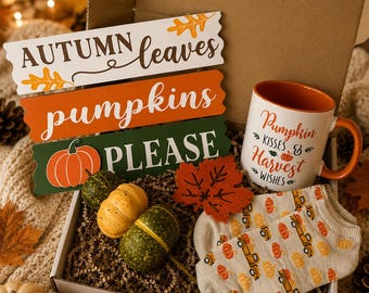 May include: A gift box containing three stacked wooden signs reading AUTUMN leaves, pumpkins, and PLEASE with a pumpkin graphic. Includes a white mug with an orange interior and the text Pumpkin Kisses & Harvest Wishes, two small gourds, and socks.