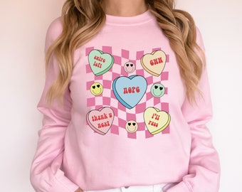 May include: Pink sweatshirt with a checkered pattern and hearts with different phrases, including "swipe left", "exxh", "nope", "thank u next", and "i'll pass".