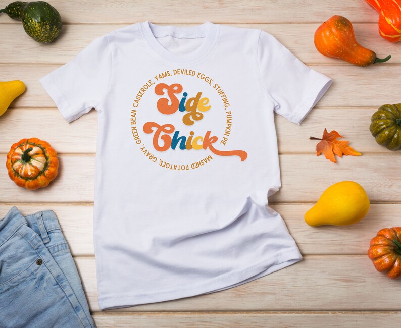 K&ouml;nnte beinhalten: Wei&szlig;es T-Shirt mit einem Grafikdesign, das "Side Chick" in einer Retro-Schriftart sagt. Die Grafik ist von einem Kreis aus Text umgeben, der verschiedene Thanksgiving-Beilagen auflistet.