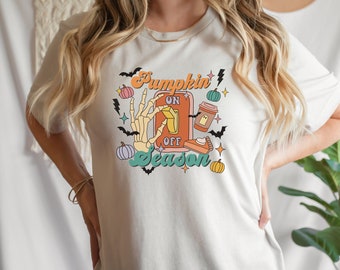 May include: White t-shirt with a graphic design of a light switch with the words "Pumpkin Season" and the switch flipped to "on". The graphic also includes a skeleton hand, a pumpkin, a pie, and a coffee cup.